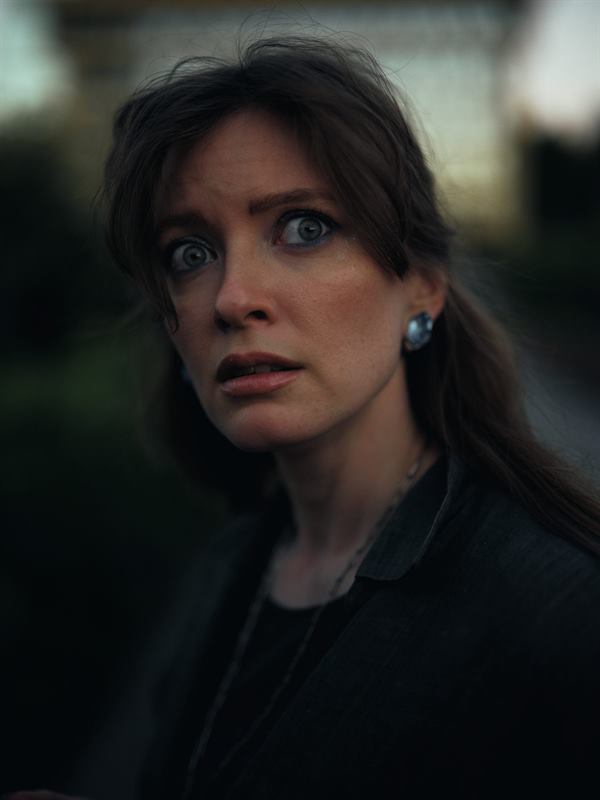 A close portrait of a woman looking past the camera, eyes wide