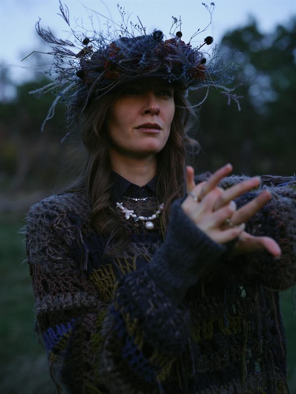 A woman in a dried flower crown reaching a hand towards the camera