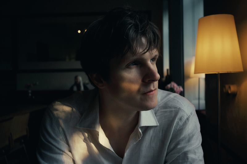 A young man in a white shirt in lamplight, turning towards the window