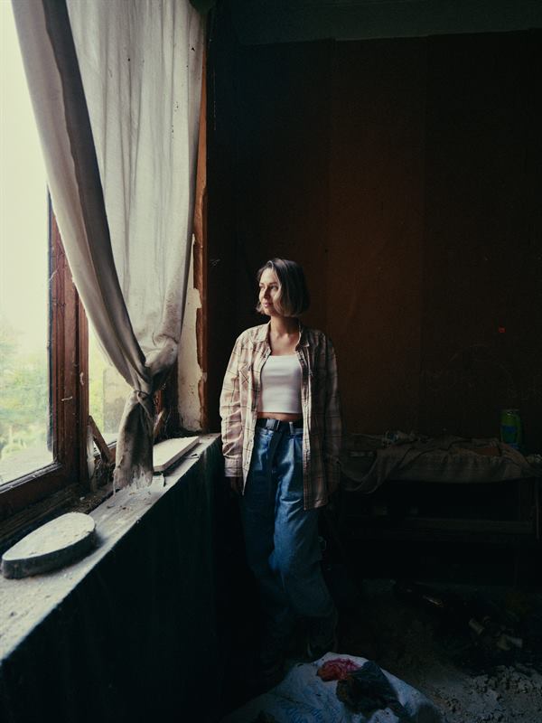 A woman standing at a bright window in a bare room
