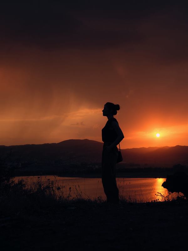 A woman in silhouette watching the sun set over a lake