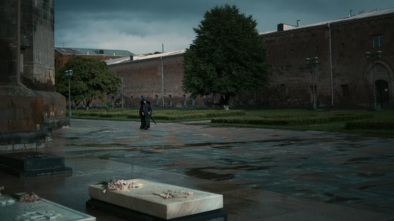 A figure in black crossing a wet courtyard beside a brick monastery
