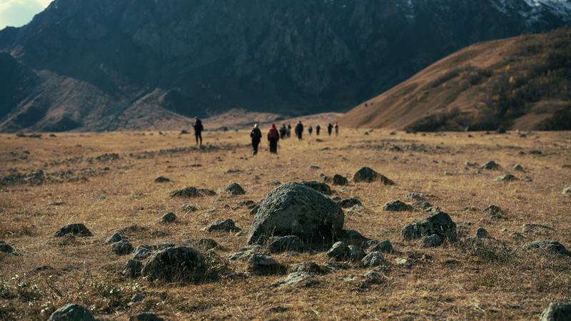 A line of walkers crossing a stony plateau below the mountains