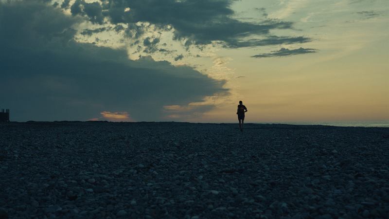 A figure walking a pebble beach at sunset