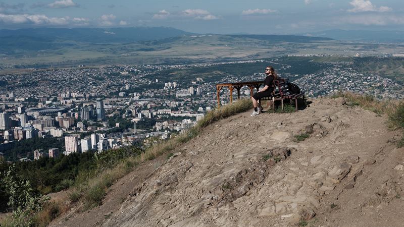 A figure resting on a bench on a ridge above a whole city